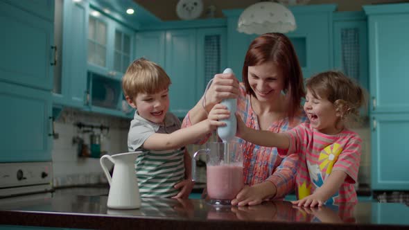 Happy family of mother and two kids cooking smoothie with blender