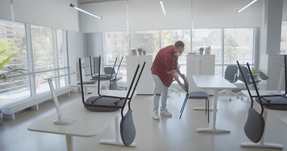 Young Man in Safety Mask Putting Chairs Down in Open Space Office