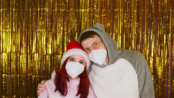 Woman and Man in Medical Masks on Background of Shimmering Golden Tinsel