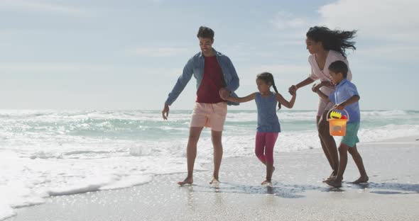 Happy hispanic mother, father, son and daughter playing in sea at the beach