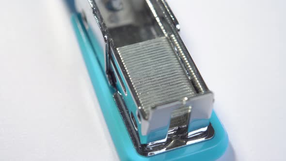 Office stapler loaded with metal staples on a white table. Macro