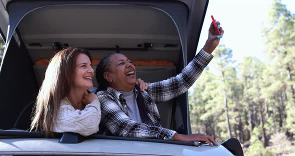 Mature multiracial women taking a selfie with smartphone inside mini van camper roof