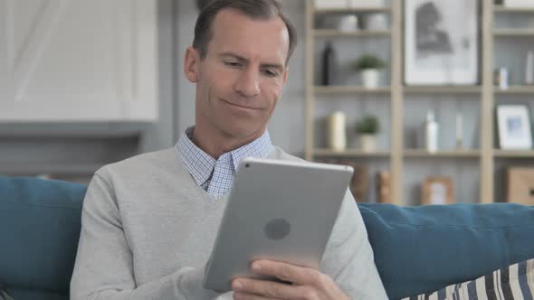 Middle Aged Man Using Tablet While Relaxing on Couch