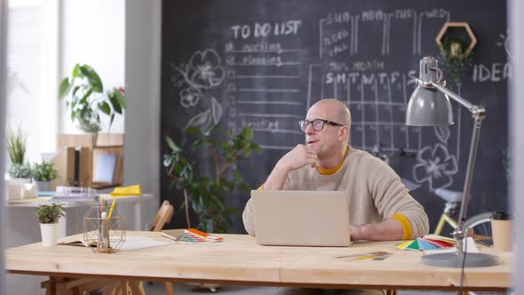 Bald Businessman in Glasses Working on Laptop in Office