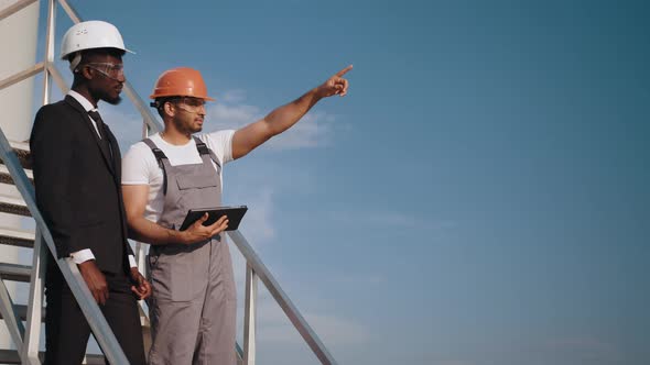 Indian Engineer in Orange Helmet and Grey Overalls Pointing in Distance and