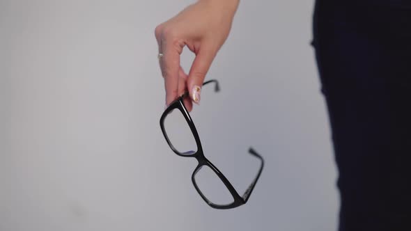 female hand is holding model of eyeglasses with black rim on a gray background