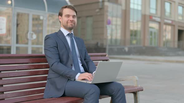 Businessman Shaking Head in Approval While using Laptop Sitting Outdoor on Bench