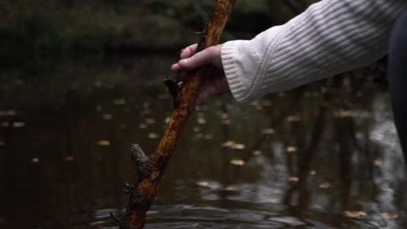 Hand relaxing with stick near rippling water side medium shot