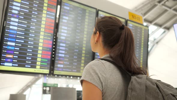 Brunette Looks at Departures Schedule in Airport Terminal