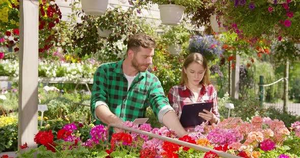 Two Gardeners Doing Paperwork Between Plants