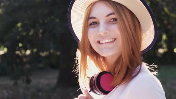 Portrait of pretty positive teenage girl with red hair wearing straw hat and pink earphones 