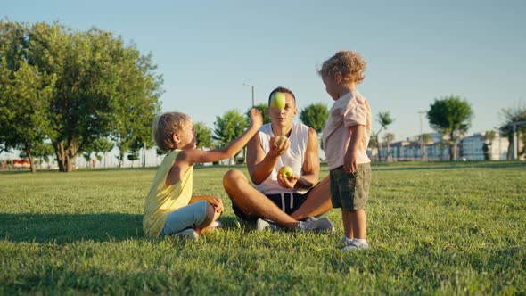 Happy Father Juggling with Green Apples in the Park with His Kids