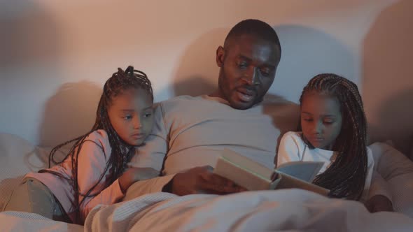 Father Reading Book to Daughters in Bed