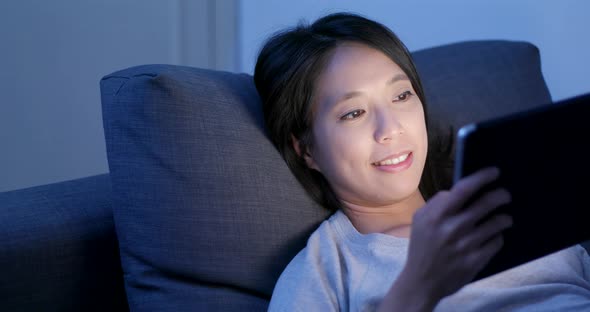 Woman use of tablet computer and lying on sofa at night