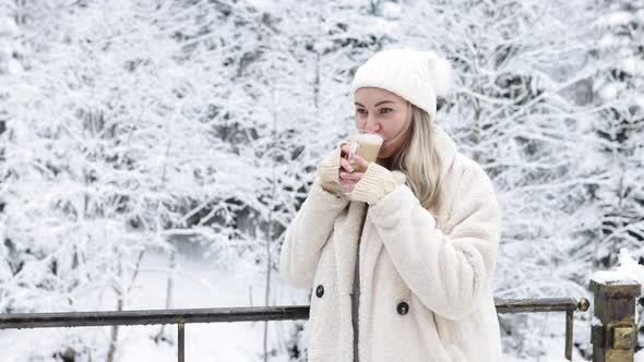 A Girl in Warm Fashionable Clothes Drinks Coffee Outside in Winter