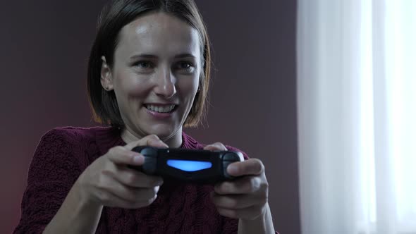 Happy smiling woman holding controller of game console and playing online games