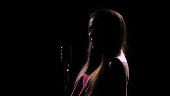 Side View of a Young Attractive Woman Who Sings Sexually Into a Vintage Microphone. Shot in a Dark