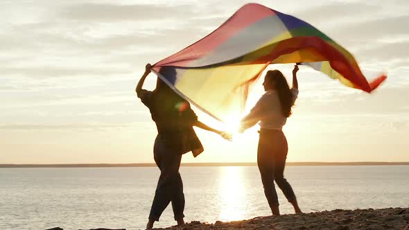 Couple standing near the sea with big rainbow flag. 