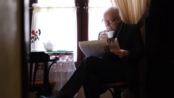 Grayhaired Grandfather is Sitting in a Cafe Drinking Tea He is Reading a Newspaper