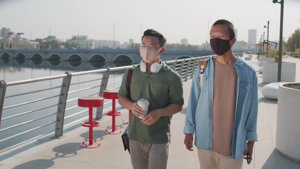 Two Asians in Face Masks Walking along Embankment