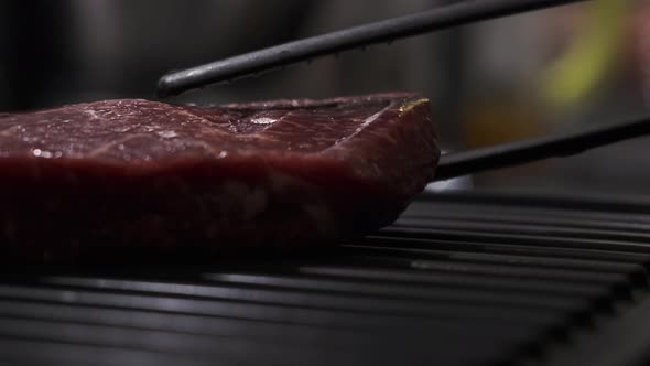 Close Up Red Beef Steak Is Placed on Home Grill Using Special Plastic Black Tongs