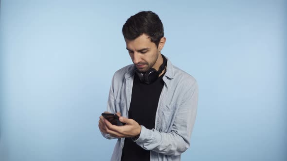 Young Confident Man Holding Phone and Scroll Screen or Typing Message Isolated on Blue Background