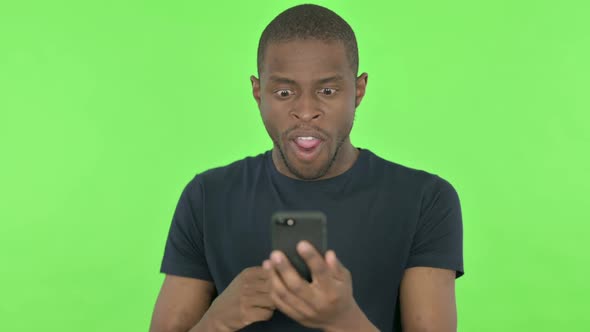 Young African Man Celebrating on Smartphone on Green Background