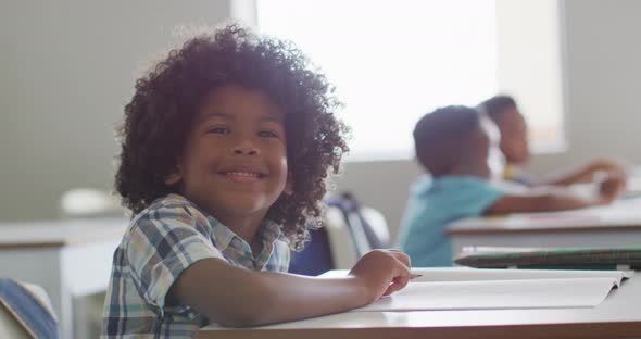 Video of happy african american boy sitting at desk during lesson in classroom