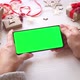 Woman holding smartphone with horizontal green screen on Christmas background - VideoHive Item for Sale