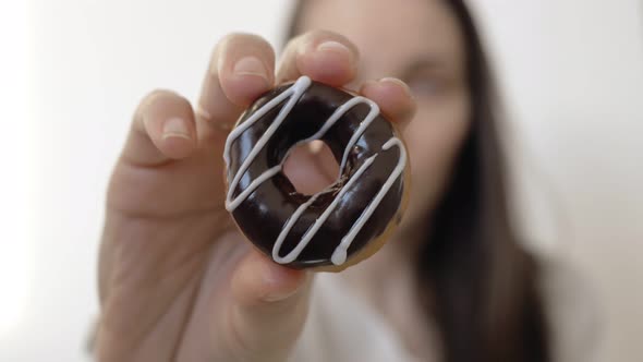 A Woman with Dark Straight Hair and Blue Eyes Holds a Lush Donut Drenched in Dark Chocolate and