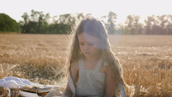 Serious Child Girl with Long Hair Sits on a Mown Wheat Field