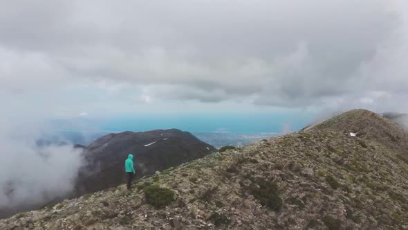 Woman walking among clouds on mountain ridge White Mountains Crete with great view