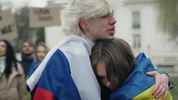 Young caucasian man with Russian flag hugging young caucasian woman with Ukrainian flag. Shot with R