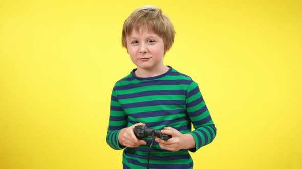 Excited Absorbed Kid Playing Game Console and Making Victory Gesture at Yellow Background