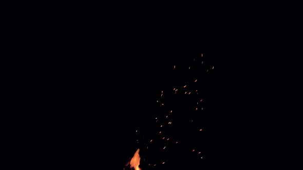 Glowing embers drift up into the darkness of the night sky from a campfire.