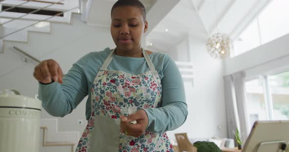 Happy african american plus size woman wearing apron, cooking in kitchen composting vegetable waste