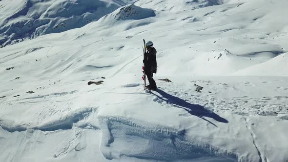 Aerial drone circling view of a skier with skis on top of a snow covered mountains in the winter.