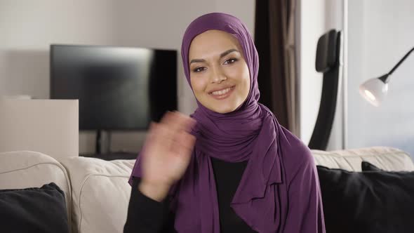 A Young Beautiful Muslim Woman Waves at the Camera with a Smile As She Sits