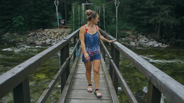 Woman Walking Along Suspension Bridge Alone in Picturesque Green Forest Setting