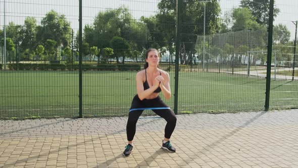 Young Sporty Woman Performs a Squat with an Elastic Band