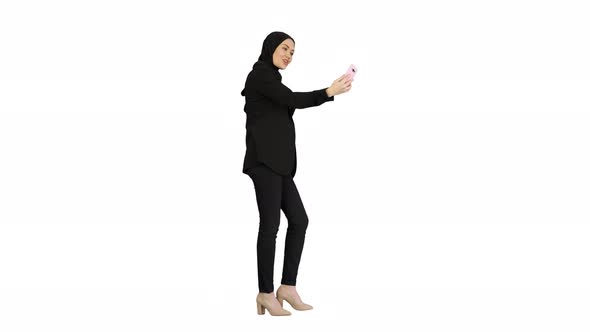 Young Pretty Muslim Woman in Hijab Having Video Call on Her Phone As She Walks on White Background