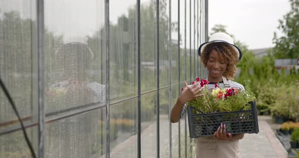 Black Woman with a Flowers Crate Standing at Plant