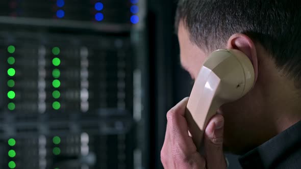 A man calls on an old phone against the backdrop of a modern server cabinet
