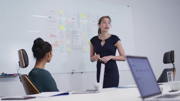 Caucasian woman giving a presentation in front of her office colleagues in meeting room at office