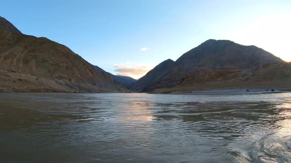 the confluence and convergence of river zanskar and indus with mountains and sun in the background.