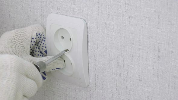 Electrician's Hands with a Screwdriver Fix the Electrical Outlet on Wall