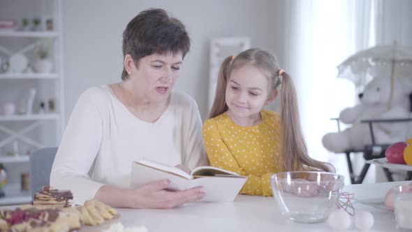 Portrait of Middle-aged Caucasian Woman and Little Girl Reading Recipes of Tasty Pancakes for