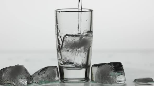 Pouring Up Shot of Vodka Into Drinking Glass. Slow Motion. White Background