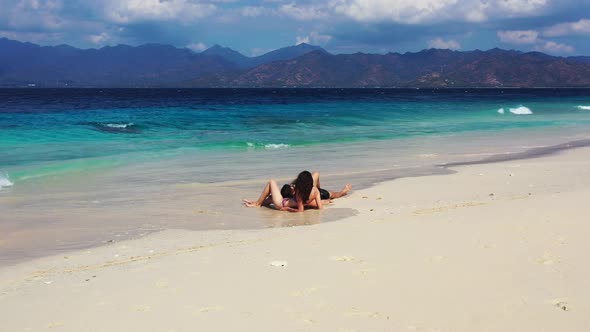 Young couple in love lying on wet white sand of exotic beach washed by waves coming from blue turquo