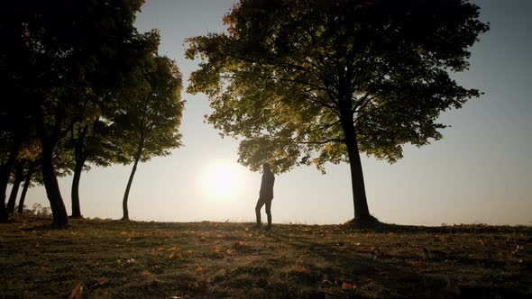 Against the Background of the Bright Orange Sunset Sky Silhouettes of a Man and Takes a Picture on